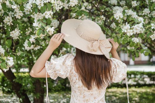 An attractive long-haired woman walks in the spring in the park of blooming apple trees. Spring portrait of a woman