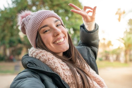 Young beautiful woman smiling taking selfie photo at university campus. Trendy girl with winter hat. Positive cheerful female student youth concept.