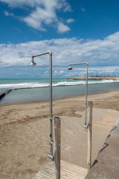 On a deserted sandy beach there are two ageing showers waiting for bathers.