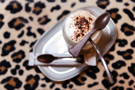 cappuccino coffee with milk foam and a chocolate spoon on a table with leopard print, concept of coffee shop and barista art.