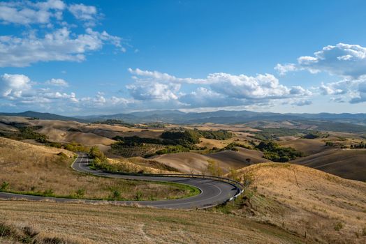 View from a hill over the typical Tuscan countryside in September with a road without cars meandering from the hill.