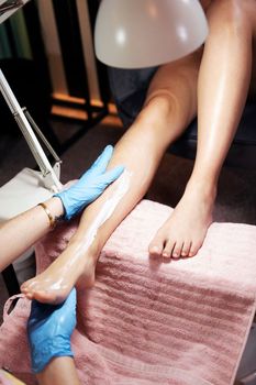 detail of the legs of a woman receiving a moisturizing foot and leg massage after her pedicure treatment at the beauty salon, wellness and body care concept