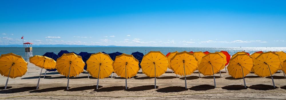 A series of orange umbrellas awaits the first bathing fear of the day on a beautiful sandy beach by the sea.