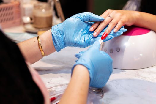 detail of a beautician's hands testing nail polish colors on her client's hands during a manicure treatment, concept of wellness and body care