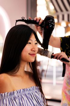 hair stylist combing with brush and dryer the straight hair of a young asian woman in the hairdressing salon, beauty care and wellness concept