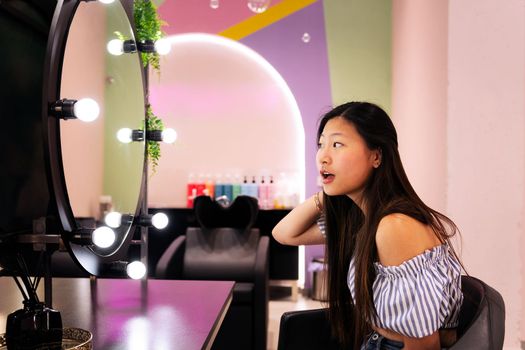 beautiful young woman admires surprised her new haircut and hairstyle in the hairdresser's salon mirror, beauty care and wellness concept