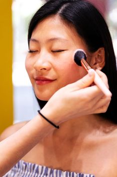 portrait of a young woman receiving a professional makeup with a brush in a beauty salon, concept of wellness and body care