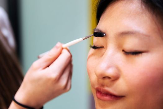 professional makeup artist combing and making up the eyebrows of a beautiful young woman, concept of wellness and beauty care