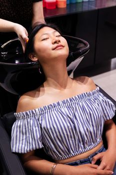 young asian woman washing her hair at the beauty salon hairdressing zone, concept of wellness and hair care