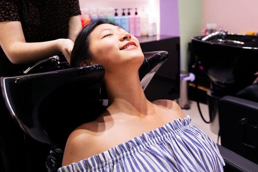 young asian woman washing her hair at the beauty salon hairdressing zone, concept of wellness and hair care