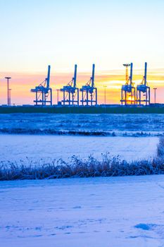 Industrial area cranes and container harbor with beautiful grassland and dike dyke nature seascape panorama in Weddewarden Bremerhaven Bremen Germany.