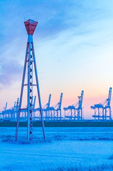 Shipyard cranes shipyard crane and container port with cold and snow in winter at sunset in Weddewarden Bremerhaven Germany.