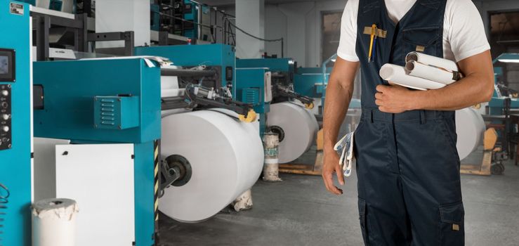 Man working in printing house with paper and printing machine