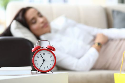 Alarm clock at seven o'clock and woman sleeping on couch. Fatigue and restful sleep concept