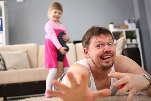 Little smiling girl holds father the leg, is lying on floor. Home fun games with kids concept