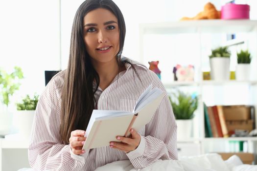 Beautiful woman is sitting on bed and holding diary. Reading book or planning day concept