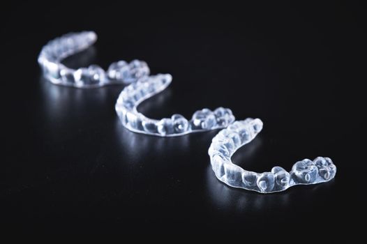 Three transparent aligners lie in a row on a black background. No people.