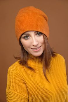 Portrait of a beautiful young woman in orange, in a sweater and a hat smiling, studio.