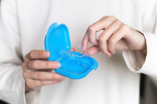 Close-up of a plastic transparent brace in the hand of a young woman, with a blue storage box. Selective focus.