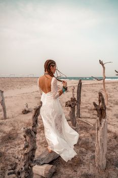 Model in boho style in a white long dress and silver jewelry on the beach. Her hair is braided, and there are many bracelets on her arms