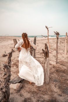 Model in boho style in a white long dress and silver jewelry on the beach. Her hair is braided, and there are many bracelets on her arms