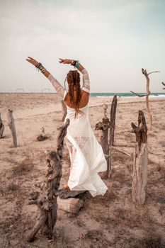 Model in boho style in a white long dress and silver jewelry on the beach. Her hair is braided, and there are many bracelets on her arms