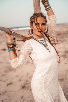 Model in boho style in a white long dress and silver jewelry on the beach. Her hair is braided, and there are many bracelets on her arms