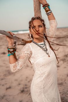 Model in boho style in a white long dress and silver jewelry on the beach. Her hair is braided, and there are many bracelets on her arms