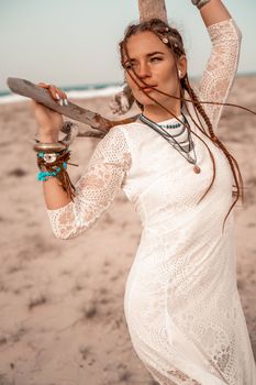 Model in boho style in a white long dress and silver jewelry on the beach. Her hair is braided, and there are many bracelets on her arms