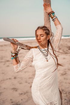 Model in boho style in a white long dress and silver jewelry on the beach. Her hair is braided, and there are many bracelets on her arms