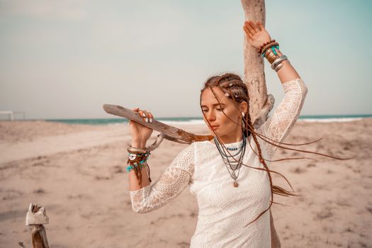 Model in boho style in a white long dress and silver jewelry on the beach. Her hair is braided, and there are many bracelets on her arms