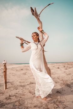 Model in boho style in a white long dress and silver jewelry on the beach. Her hair is braided, and there are many bracelets on her arms