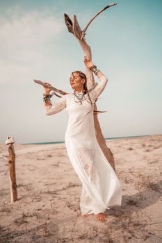 Model in boho style in a white long dress and silver jewelry on the beach. Her hair is braided, and there are many bracelets on her arms