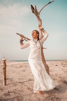 Model in boho style in a white long dress and silver jewelry on the beach. Her hair is braided, and there are many bracelets on her arms