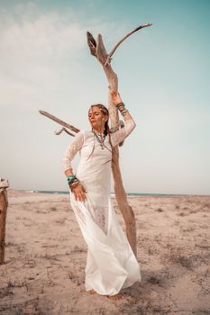 Model in boho style in a white long dress and silver jewelry on the beach. Her hair is braided, and there are many bracelets on her arms