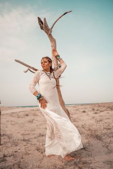 Model in boho style in a white long dress and silver jewelry on the beach. Her hair is braided, and there are many bracelets on her arms