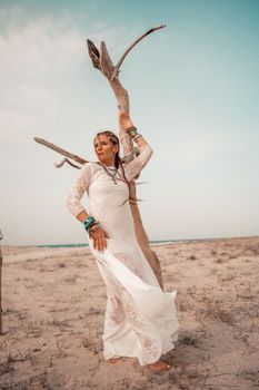 Model in boho style in a white long dress and silver jewelry on the beach. Her hair is braided, and there are many bracelets on her arms