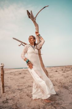 Model in boho style in a white long dress and silver jewelry on the beach. Her hair is braided, and there are many bracelets on her arms