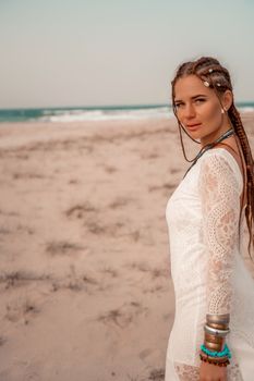 Model in boho style in a white long dress and silver jewelry on the beach. Her hair is braided, and there are many bracelets on her arms