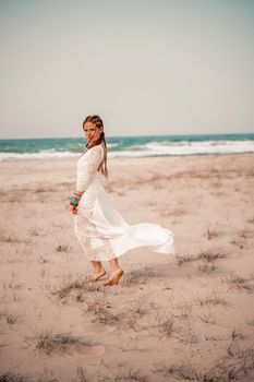 Model in boho style in a white long dress and silver jewelry on the beach. Her hair is braided, and there are many bracelets on her arms