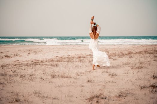 Model in boho style in a white long dress and silver jewelry on the beach. Her hair is braided, and there are many bracelets on her arms