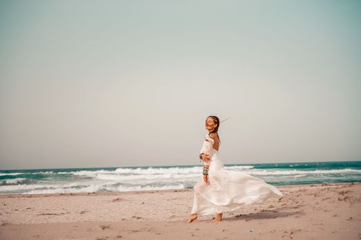 Model in boho style in a white long dress and silver jewelry on the beach. Her hair is braided, and there are many bracelets on her arms