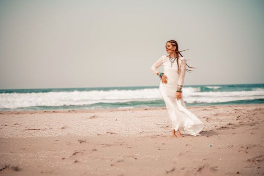 Model in boho style in a white long dress and silver jewelry on the beach. Her hair is braided, and there are many bracelets on her arms