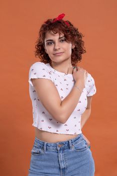 Beautiful girl stands and looks straight into the camera. Background in solid brick color. Curly hair in chestnut color.