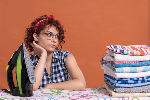 A young woman with glasses and curly hair glances at the work being done. Ironing towels on an ironing board. Isolated from the background.