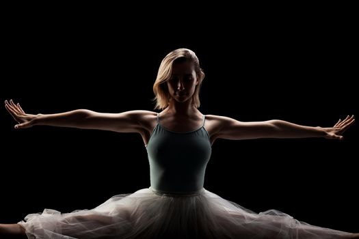 ballerina with a white dress and black top posing on black background. side lit silhouette