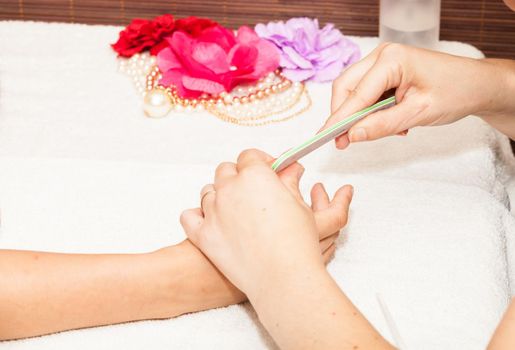 The beautician polish the client's nails before putting nail polish