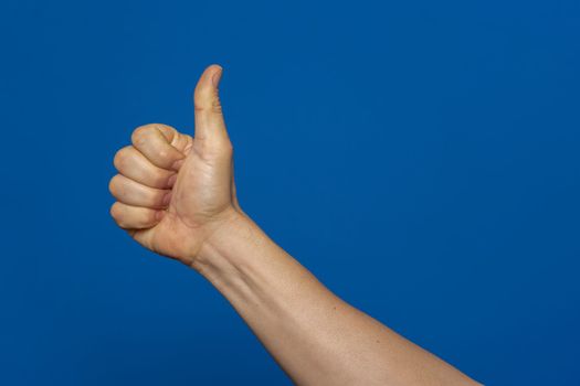 Thumb up hand sign. man's hand showing thumb up, like, ok, approval, accept, okay, good, positive hand gesture. Isolated on blue studio background