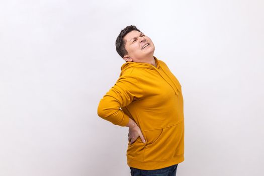 Side view of man suffering back ache, lower lumbar discomfort, painful muscle spasm, rheumatoid arthritis, pinched nerve, wearing urban style hoodie. Indoor studio shot isolated on white background.