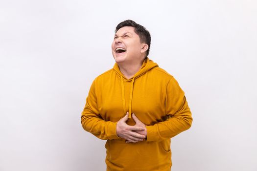 Portrait of extremely excited happy man holding his belly and laughing out loud, chuckling giggling at amusing joke, wearing urban style hoodie. Indoor studio shot isolated on white background.